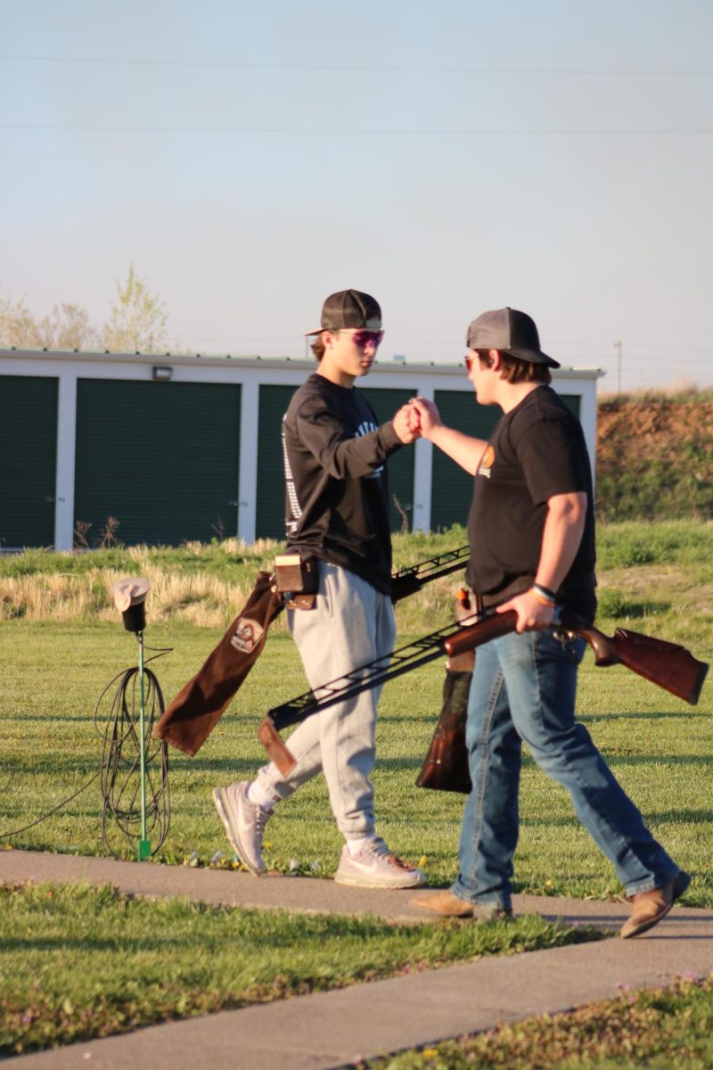 Pull. Aim. Fist Bump. Repeat. Senior Adian McKinney and sophomore Devon Helget share a fist bump as they rotate posts during a practice at Tuttle Creek Shooting Park. Every Rock Creek team member fist bumps each time they rotate.