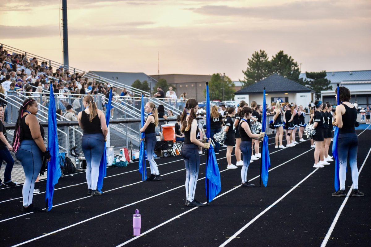 Rock Creek color guard members line up with their flags on the track during the homecoming football game, ready to perform alongside the band and cheerleaders.